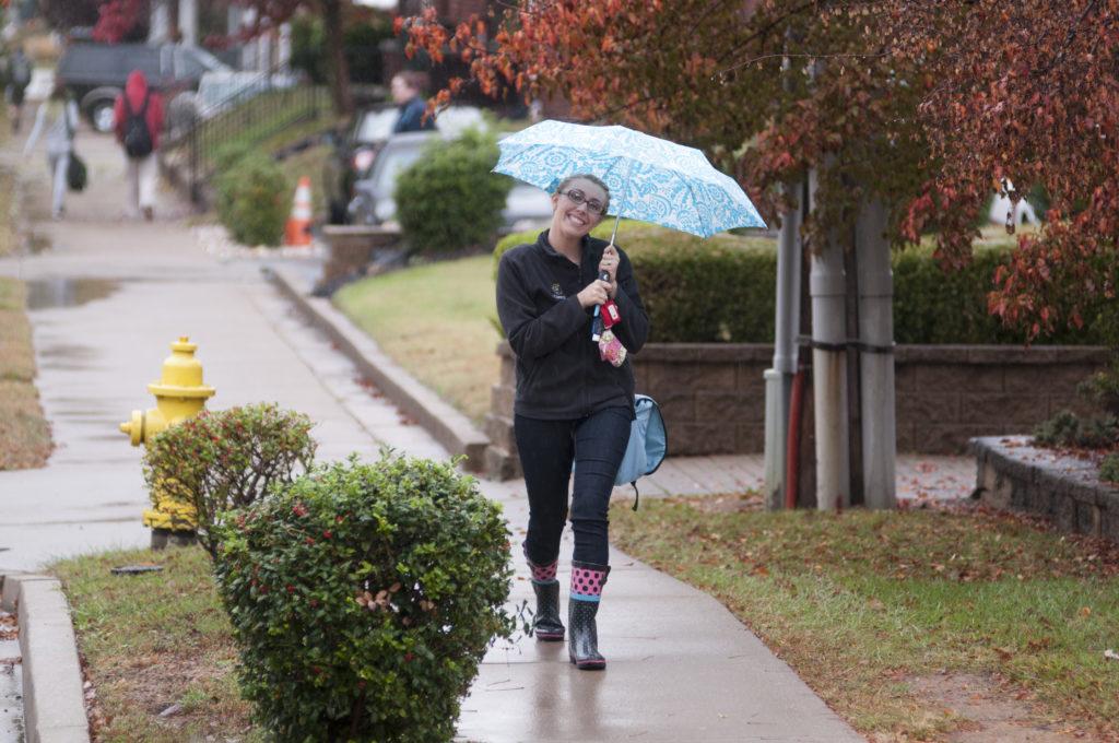 学生走在雨中，撑着伞，对着镜头微笑.